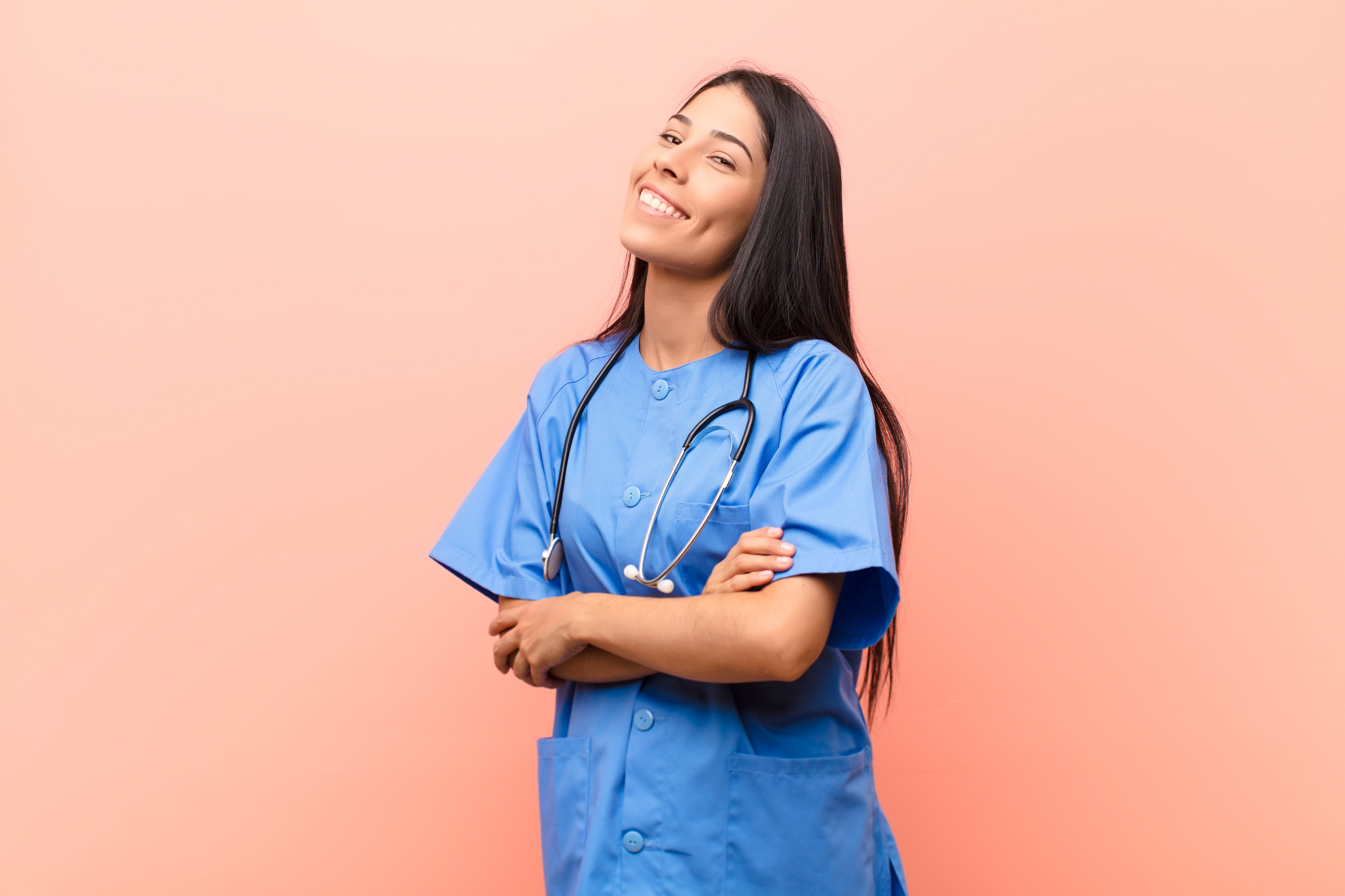 young latin nurse laughing happily with arms crossed, with a relaxed, positive and satisfied pose against pink wall