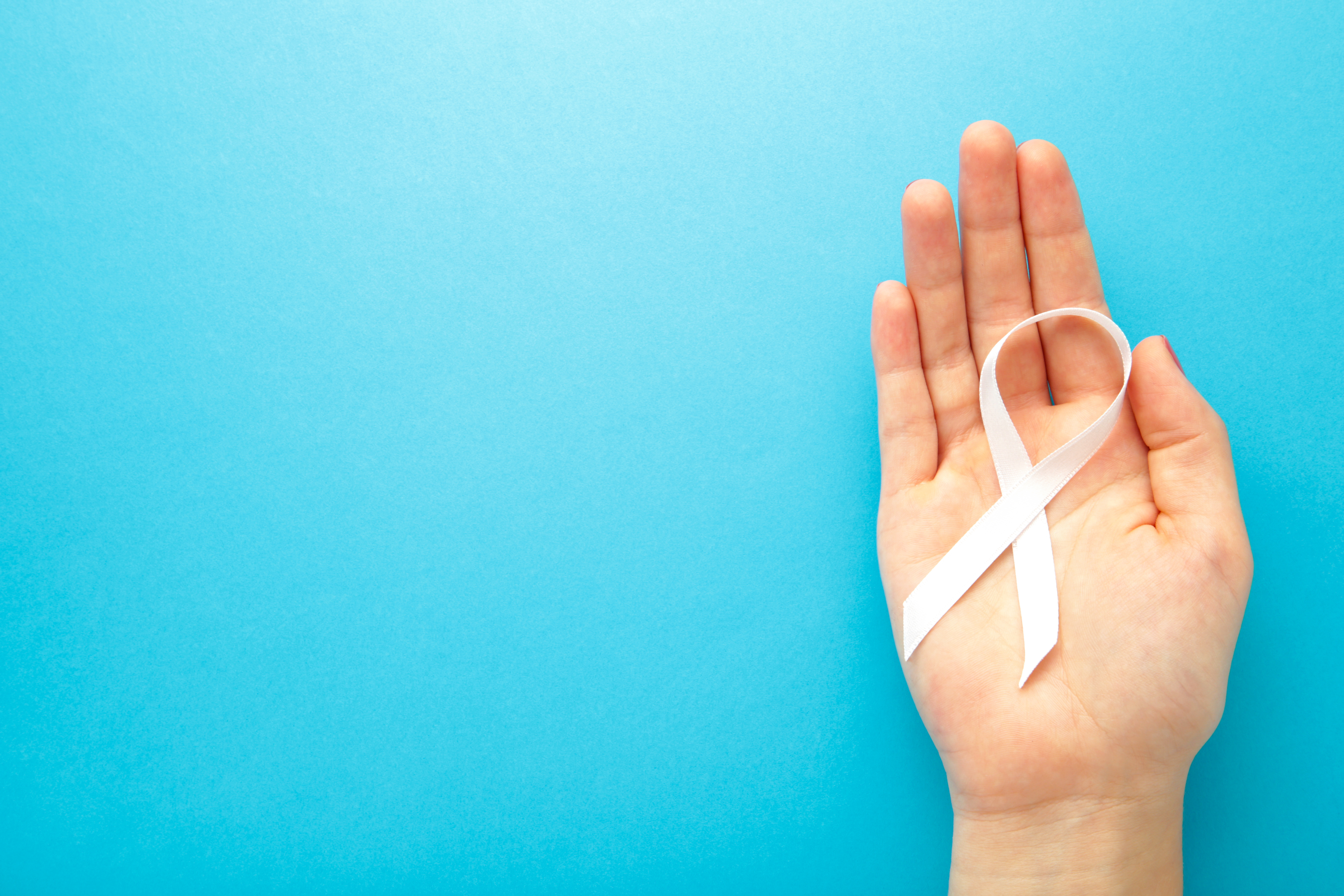 Hand holding white ribbon on blue background. Concept lung cancer awareness. Top view